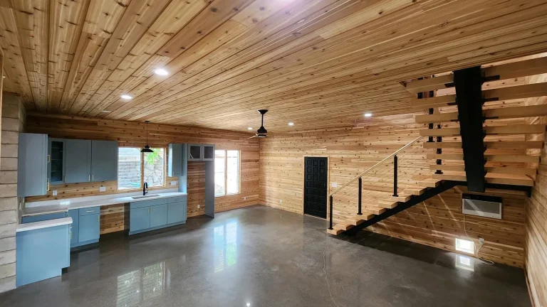Cedar-lined living space with blue cabinetry kitchenette, floating stair and polished concrete floor