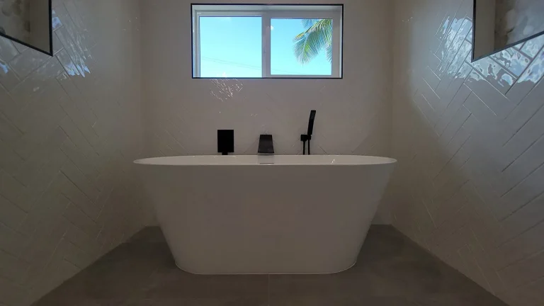 Freestanding soaking tub beneath a window with white herringbone wall tile
