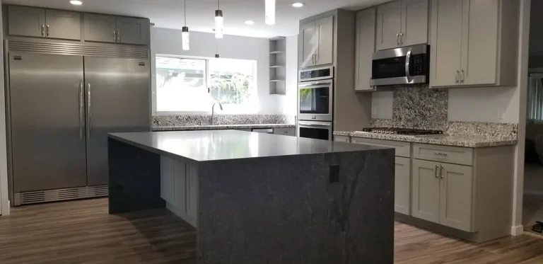 Kitchen with a dark stone waterfall island, gray shaker cabinetry and stainless appliances
