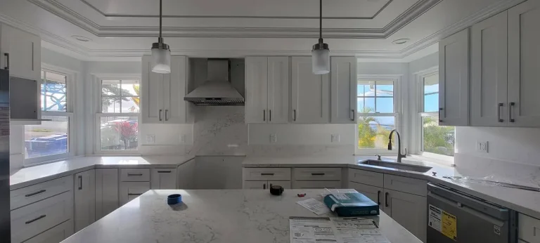 White kitchen with quartz counters and range hood during final installation